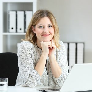 Front view portrait of a businesswoman posing looking at you on a desk at office